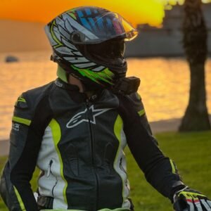Motorcyclist in gear sitting by the sea at sunset, reflecting serene beauty.